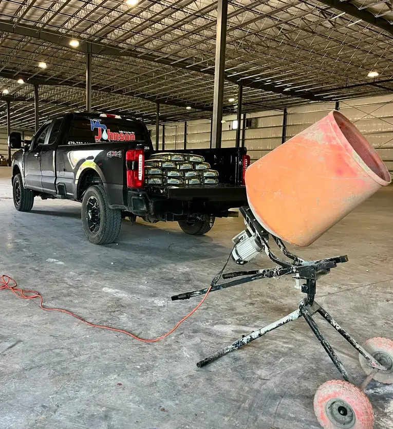 A black Johnson Plumbing F-250 loaded with concrete mix beside a mixer inside a large new commercial building