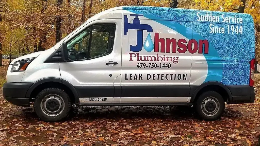 A white Johnson Plumbing van with a blue water-bubble wrap, parked side-on on autumn leaves